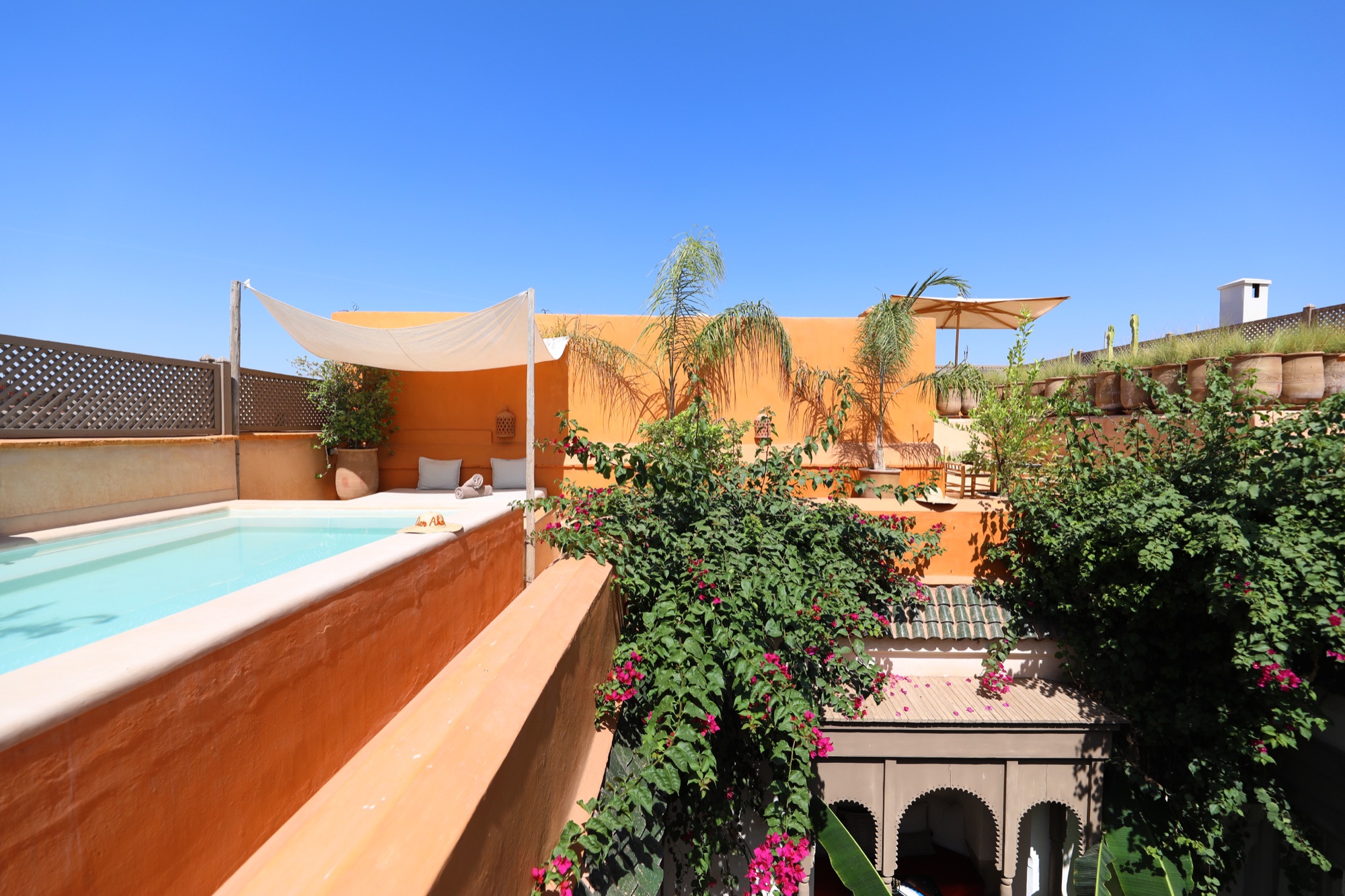 Dar Akal's rooftop pool above the green courtyard under a clear Marrakech sky
