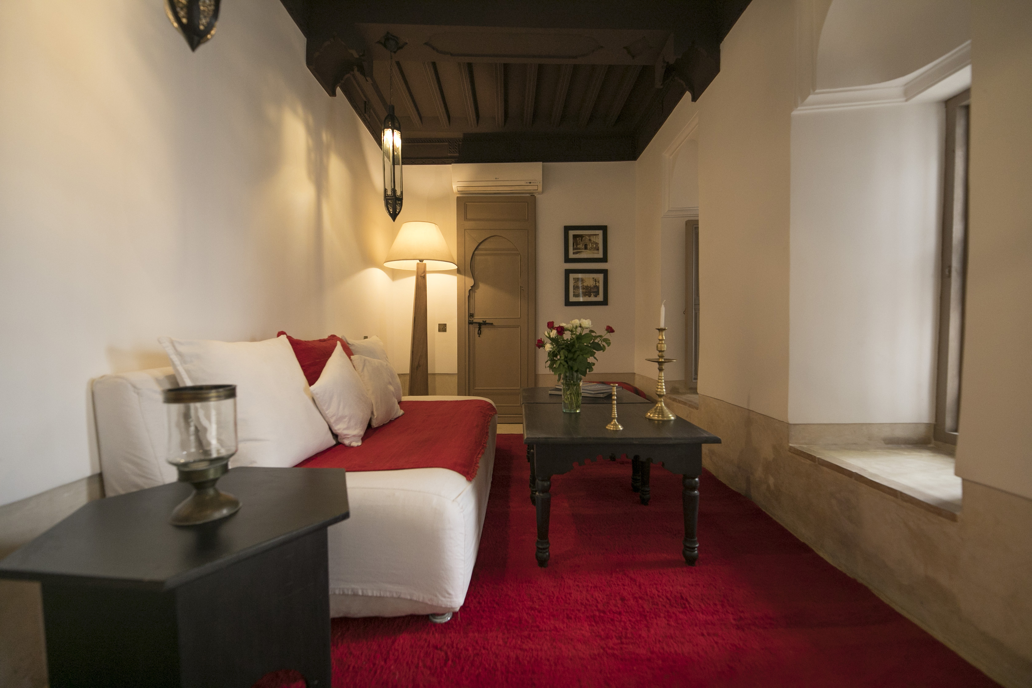 A long sitting room at Dar Akal with red textiles, flowers and warm lamplight