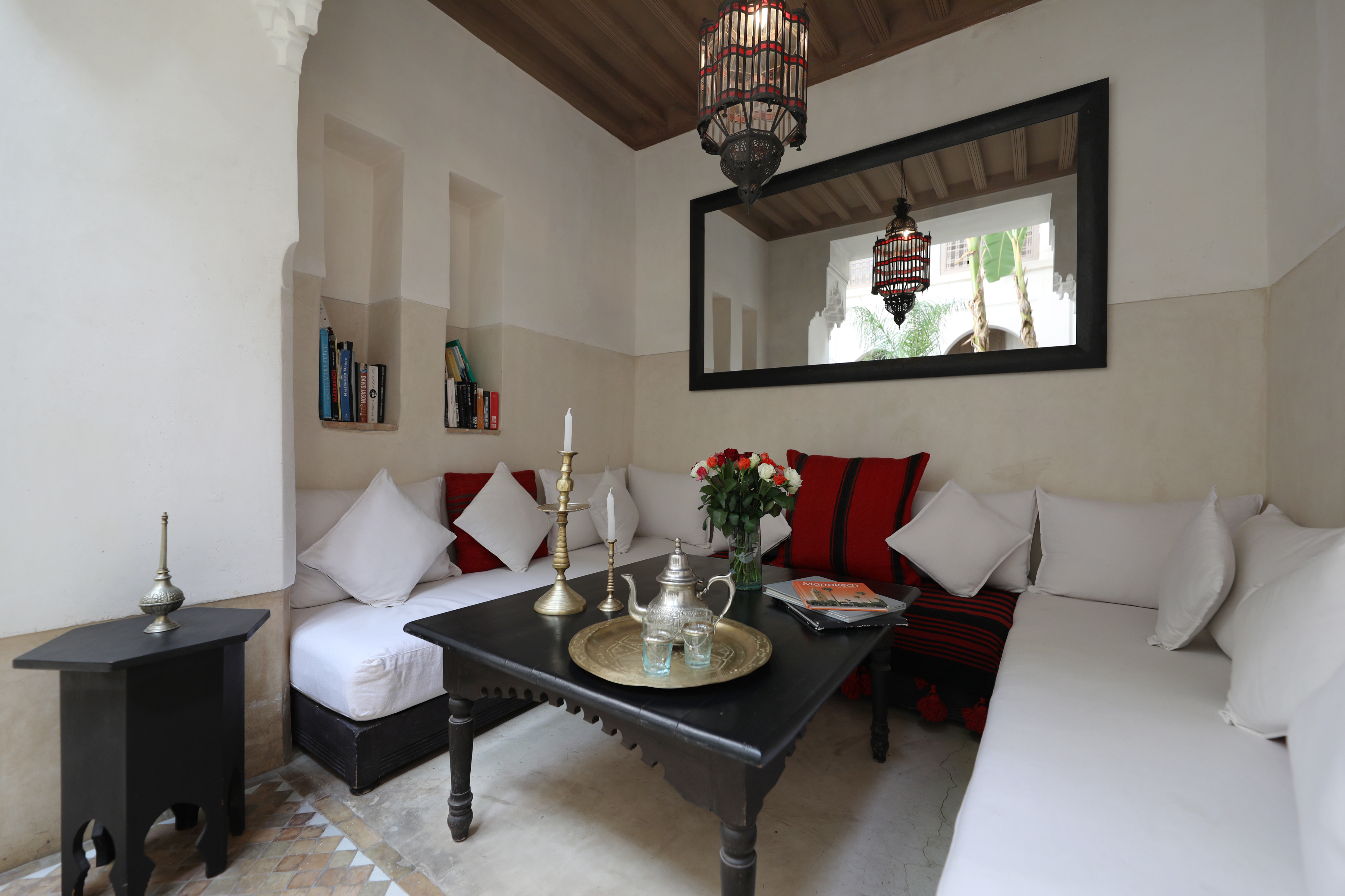 A Dar Akal sitting room with red textiles, a tea table and a mirror onto the courtyard