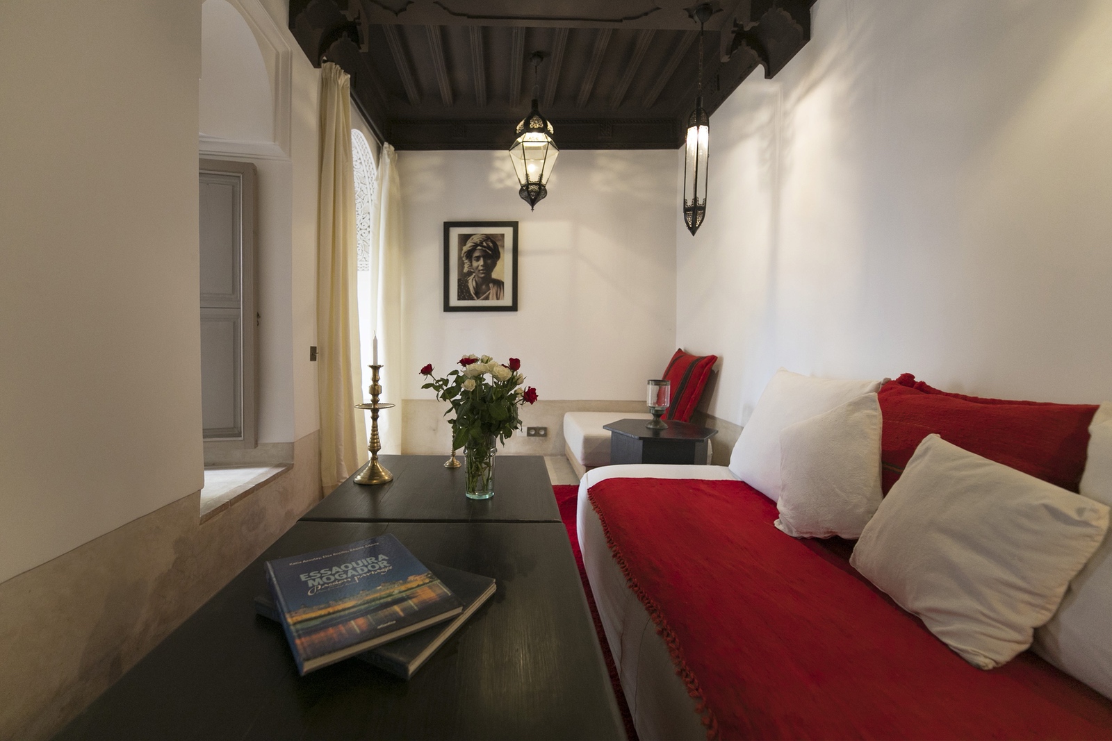 A red-and-white sitting room beneath dark timber ceilings at Dar Akal